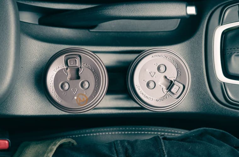 Two takeaway coffee cups standing in a car cup holders, seen from above