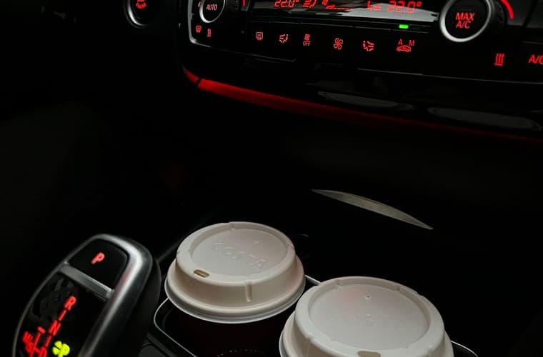 Car console with drinks in the holders and the dash display behind