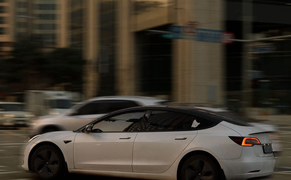 White Tesla Model 3 crossing a busy city intersection