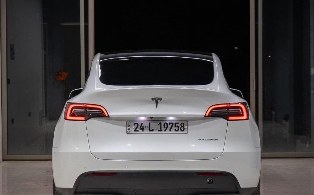 Rear three-quarter view of a white Tesla Model Y in a plain indoor showroom