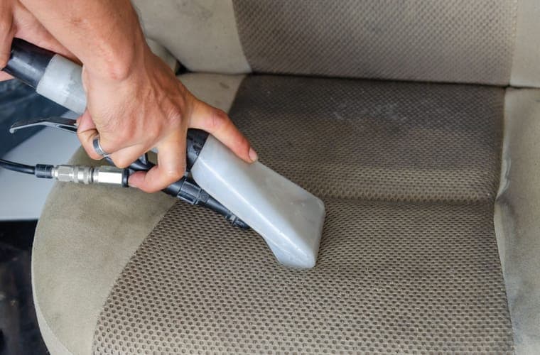 Hands vacuuming a fabric car seat