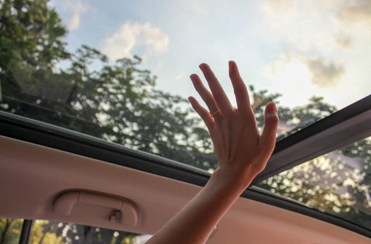 Hand reaching up to touch a car glass roof panel from inside