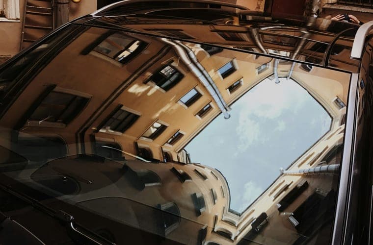 Buildings reflected in a parked car windshield in bright sun