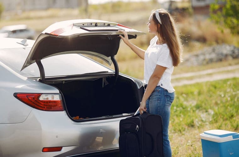 Person lifting a bag into the open rear cargo area of a car