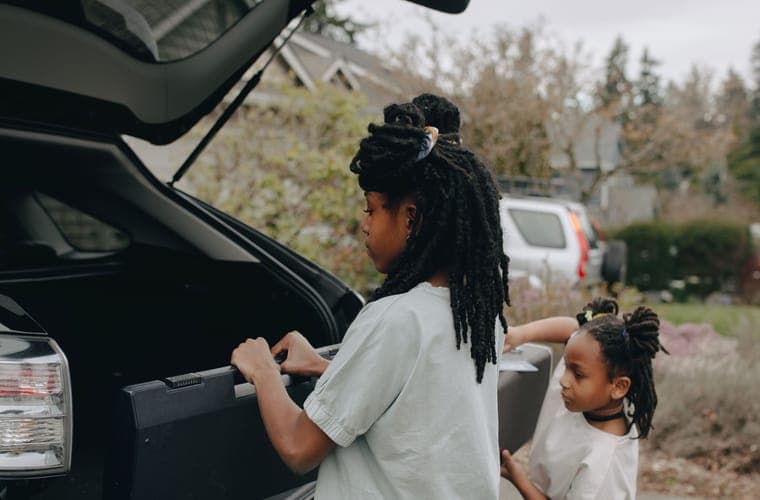 Two children lifting a suitcase into a car cargo area